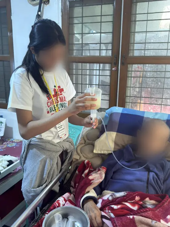 VAI student volunteers, assisting with tube feeding at the bedside, Mandalay